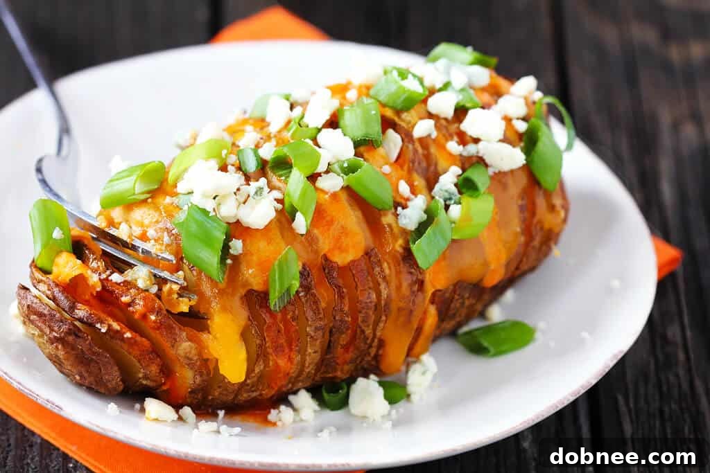 Buffalo Hasselback Potatoes in a white dish, garnished with melted cheese, blue cheese crumbles, and green onions.