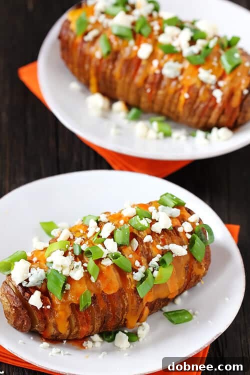 Two Buffalo Hasselback Potatoes on a light blue plate, with a spoon of sauce and a small bowl of blue cheese crumbles.