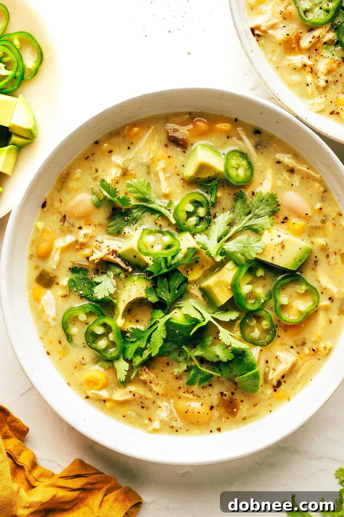 A bowl of creamy white chicken chili with various toppings, seen from above.