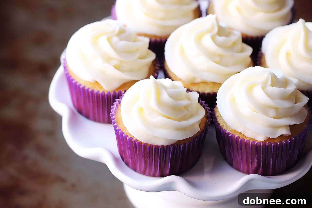 A plate of freshly baked vanilla cupcakes topped with generous swirls of vanilla buttercream frosting.