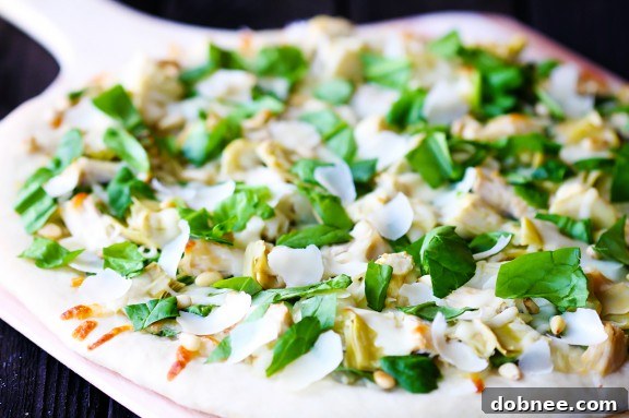 Delicious Spinach Artichoke Chicken Pizza, hot out of the oven, topped with fresh Parmesan and pine nuts.
