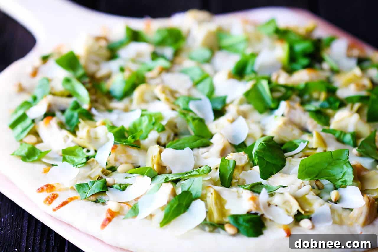 Spinach Artichoke Chicken Pizza on a wooden board.