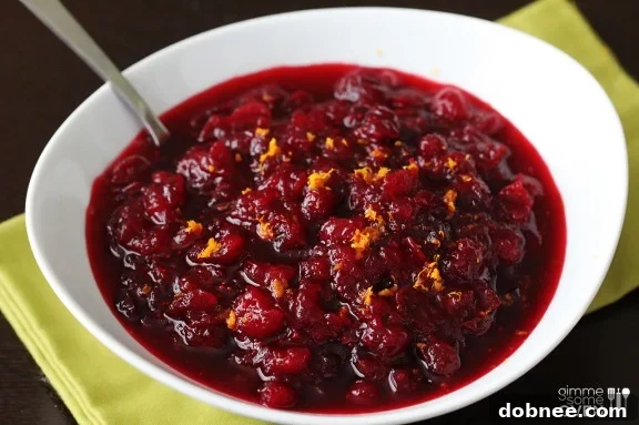 Vibrant Orange Bourbon Cranberry Sauce with orange zest garnish, served in a white bowl, perfect for holiday feasts like Thanksgiving and Christmas.