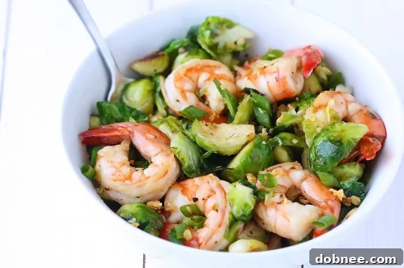 Delicious Honey Sesame Shrimp and Brussels Sprouts Stir Fry served in a bowl, garnished with green onions and sesame seeds.