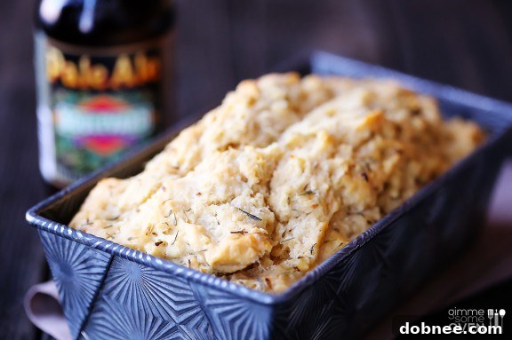 Golden-brown loaf of Whole Wheat Garlic & Herb Beer Bread on a cutting board, garnished with fresh herbs.