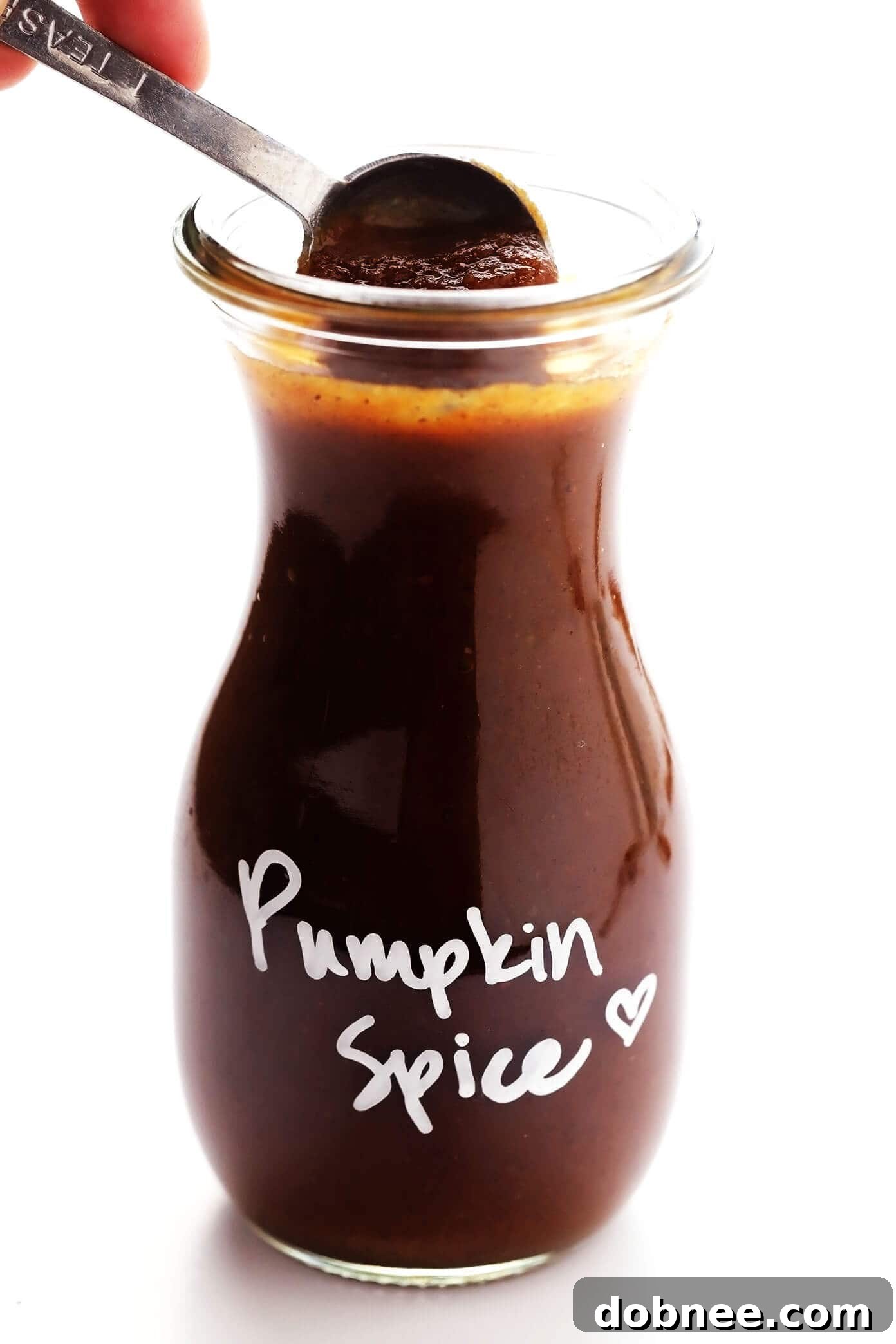 A close-up of a glass of pumpkin spice syrup, ready to be mixed into a homemade latte