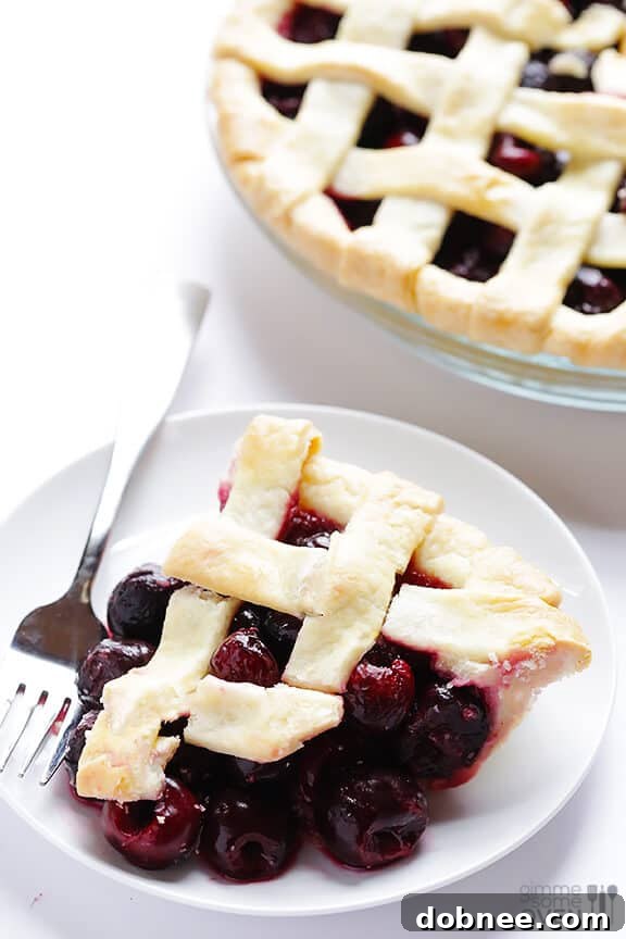 A perfect slice of sweet cherry pie, revealing a thick, juicy filling and flaky crust on a white plate