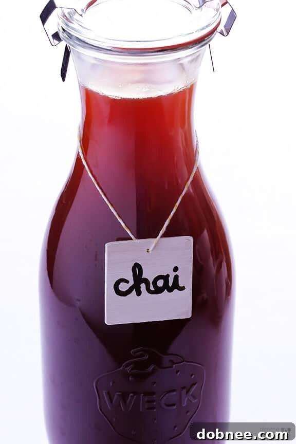 Glass bottles of homemade chai tea concentrate, ready for storage or gifting, next to a mug of chai.