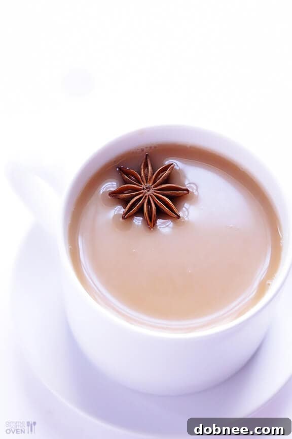 A beautifully presented hot chai tea latte in a clear glass mug, garnished with a cinnamon stick, on a rustic background.