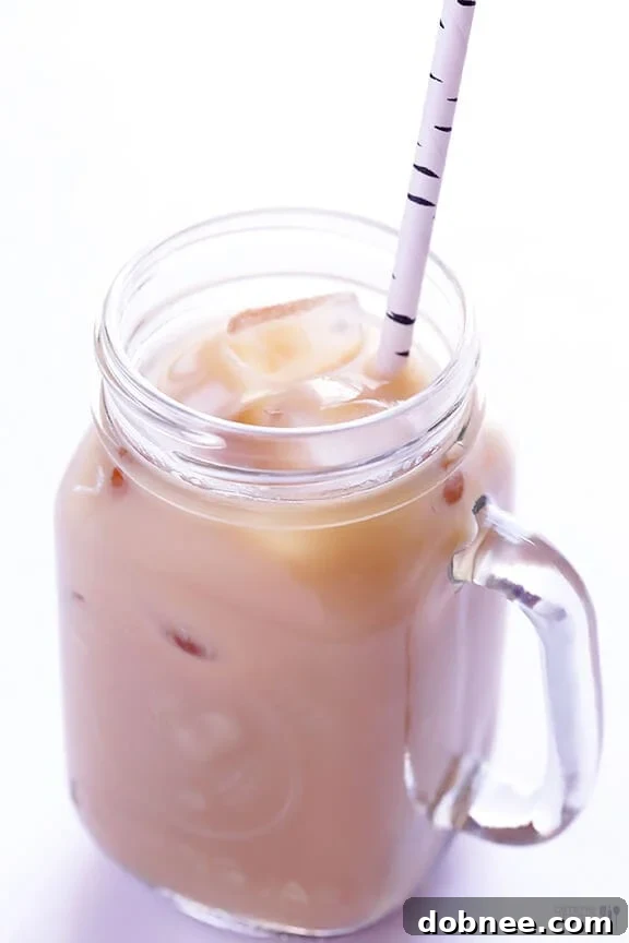 A refreshing glass of iced chai tea, filled with ice and a straw, sitting on a wooden surface.
