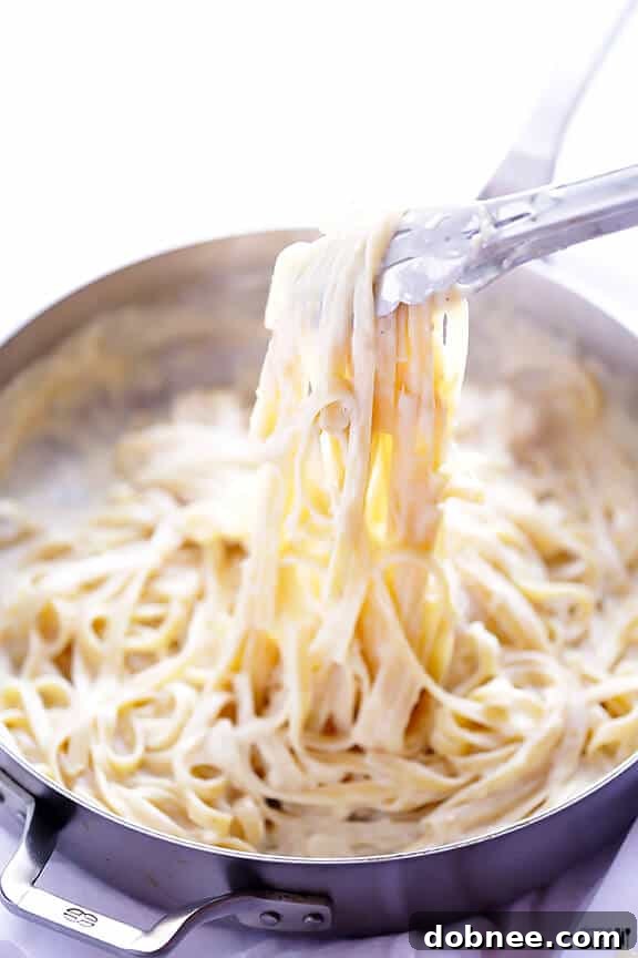 Fettuccine pasta being tossed with light alfredo sauce in a large pan.