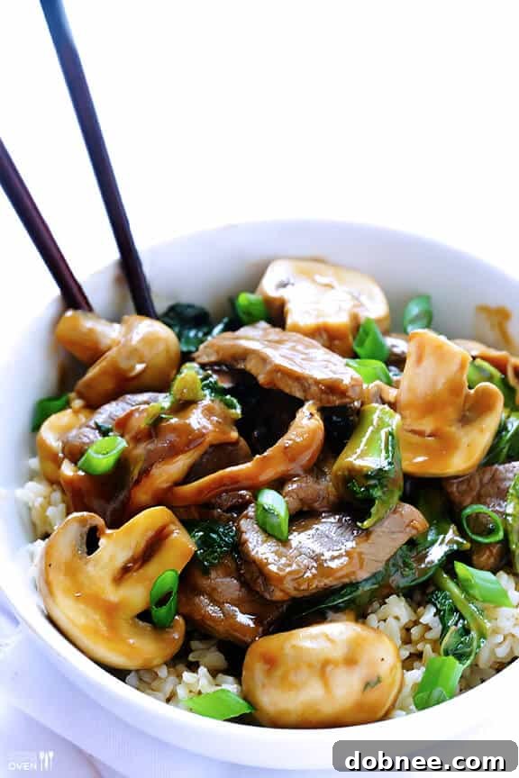 A beautifully plated bowl of Ginger Beef, Mushroom & Kale Stir-Fry, garnished with green onions and ready to be enjoyed.