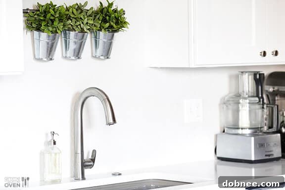 A pristine white kitchen featuring a Kohler Cape Dory cast iron sink and Sensate touchless faucet, reflecting modern design and functionality.