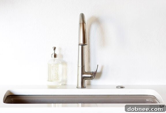 The Kohler Cape Dory cast iron sink in 'cashmere' color, beautifully installed as an under-mount, offering a subtle contrast to the white kitchen countertops.