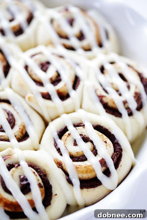 Piping cream cheese frosting generously onto warm Nutella Cinnamon Rolls