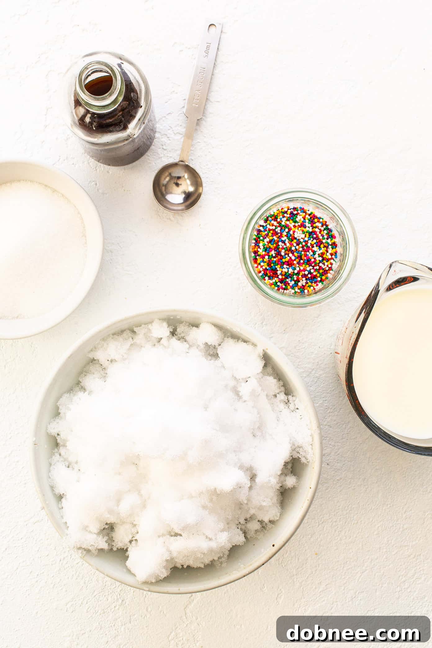 Snow Ice Cream Ingredients arranged on a table, including milk, sugar, vanilla extract, and a pinch of salt.