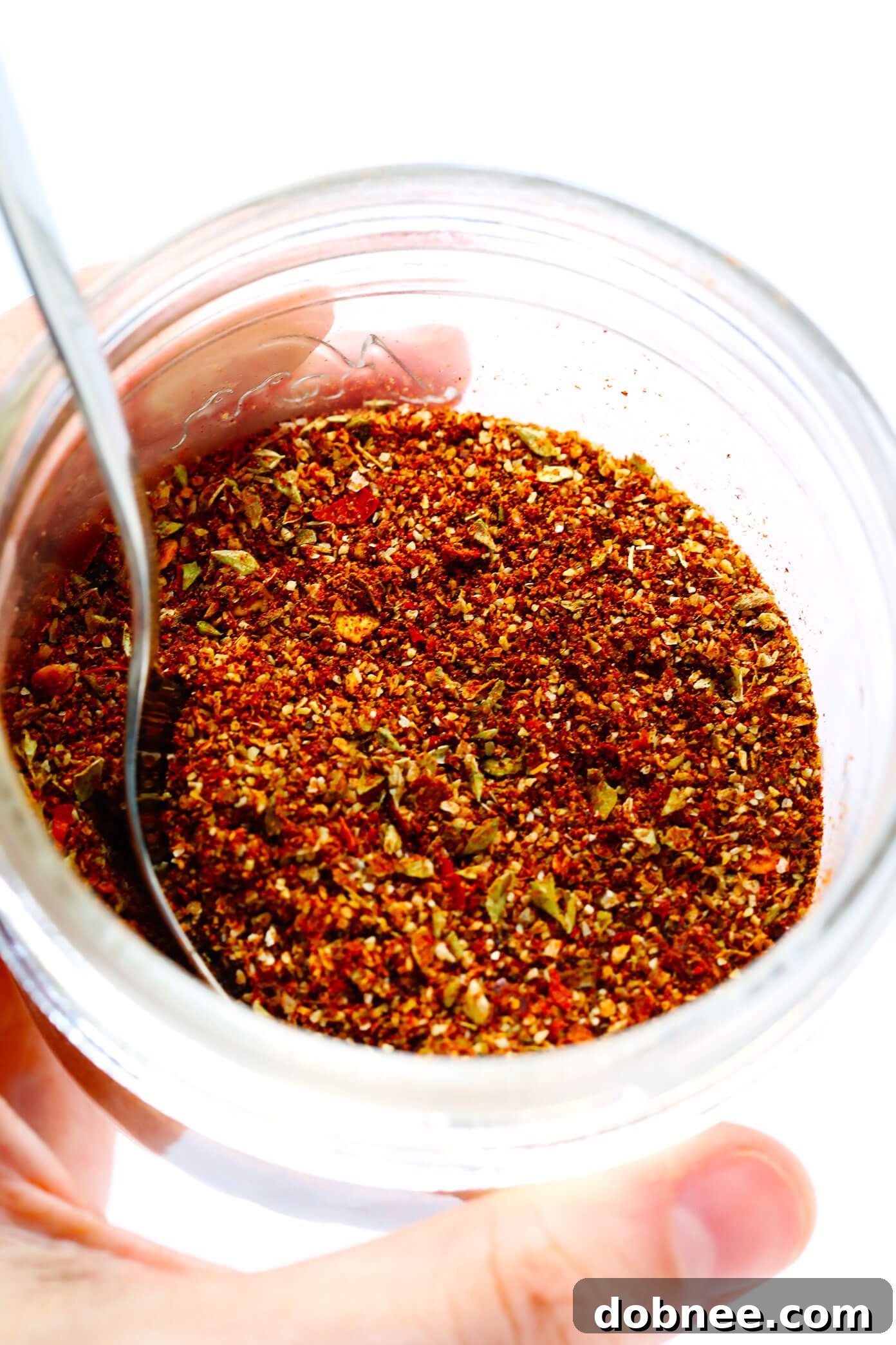 A hand stirring various spices in a bowl to create homemade taco seasoning