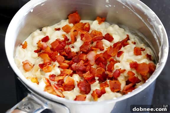 Stirring crispy bacon into the blue cheese macaroni and cheese.
