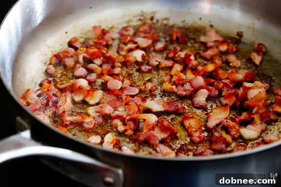 Diced bacon cooking in a skillet, creating a crispy base for mac and cheese.