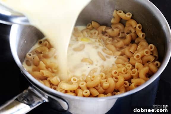 Pouring creamy sauce mixture over cooked macaroni.