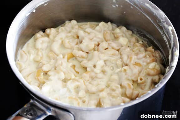 Stirring melted cheese into the macaroni, creating a creamy sauce.