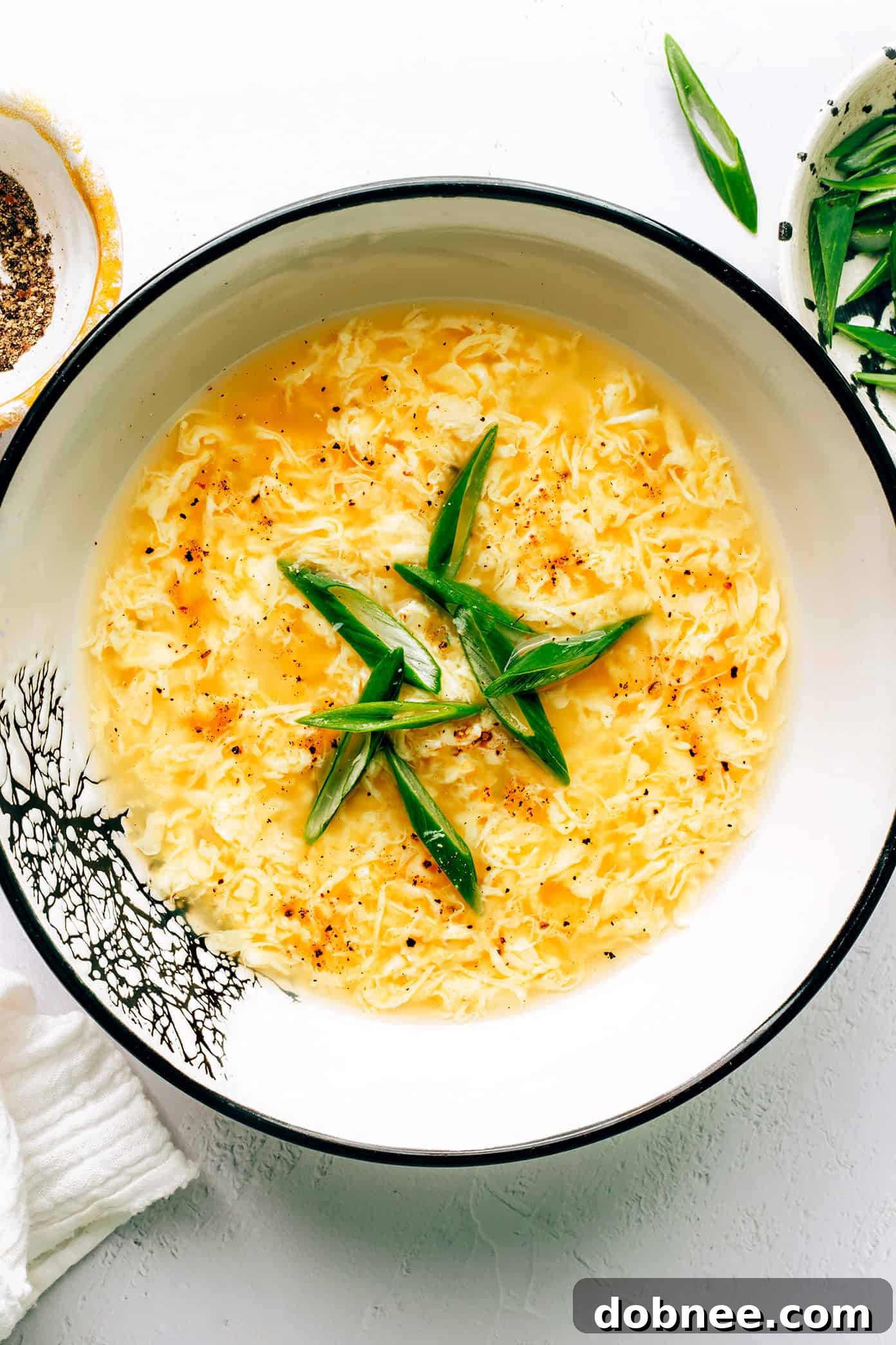 A steaming bowl of homemade Egg Drop Soup, garnished with fresh green onions.