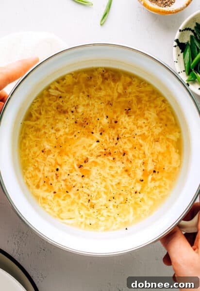 A bowl of egg drop soup with egg ribbons and green onions, accompanied by chopsticks.