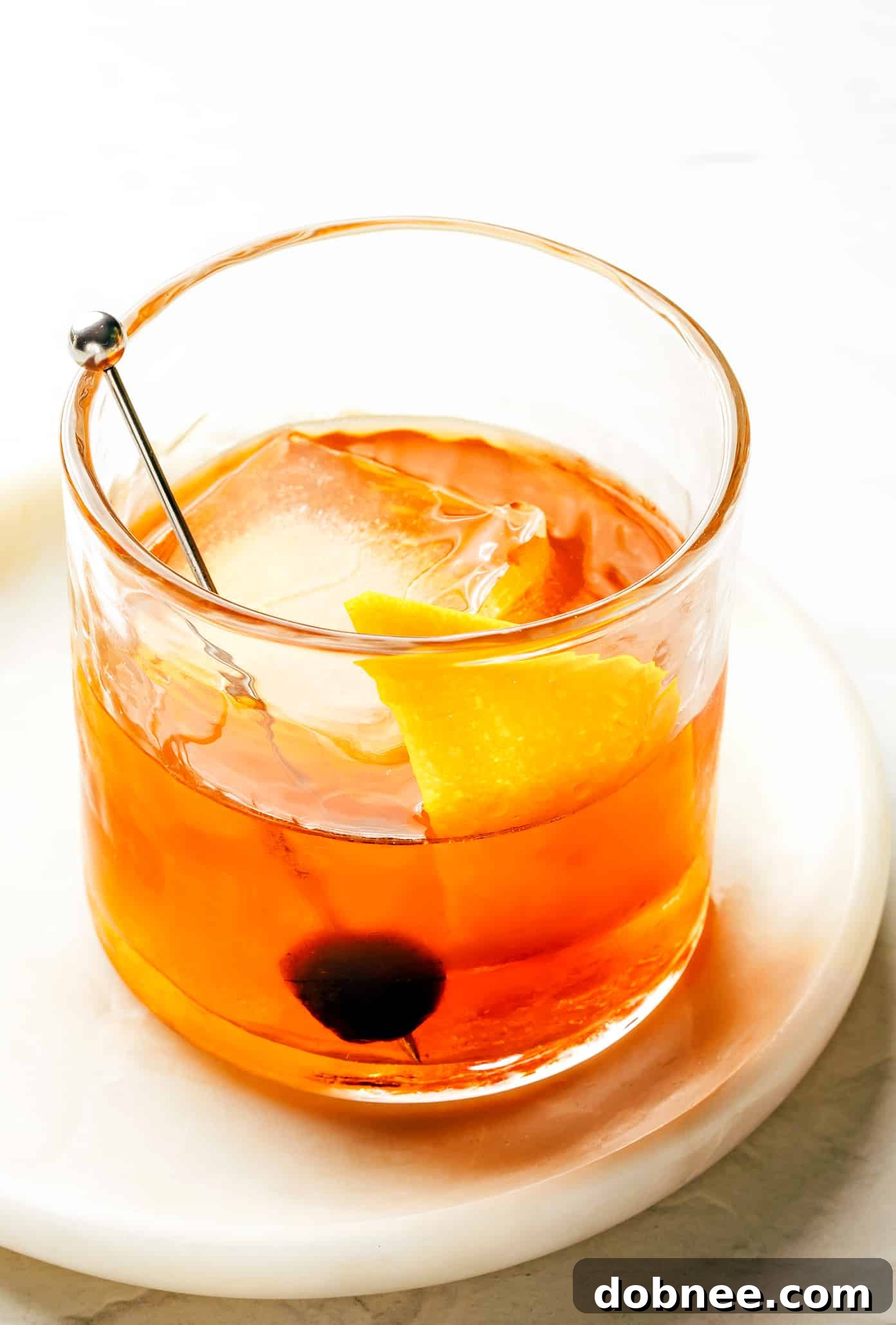 A perfectly crafted Old Fashioned cocktail with bourbon, bitters, and an orange peel, served in a classic lowball glass with a large ice cube.