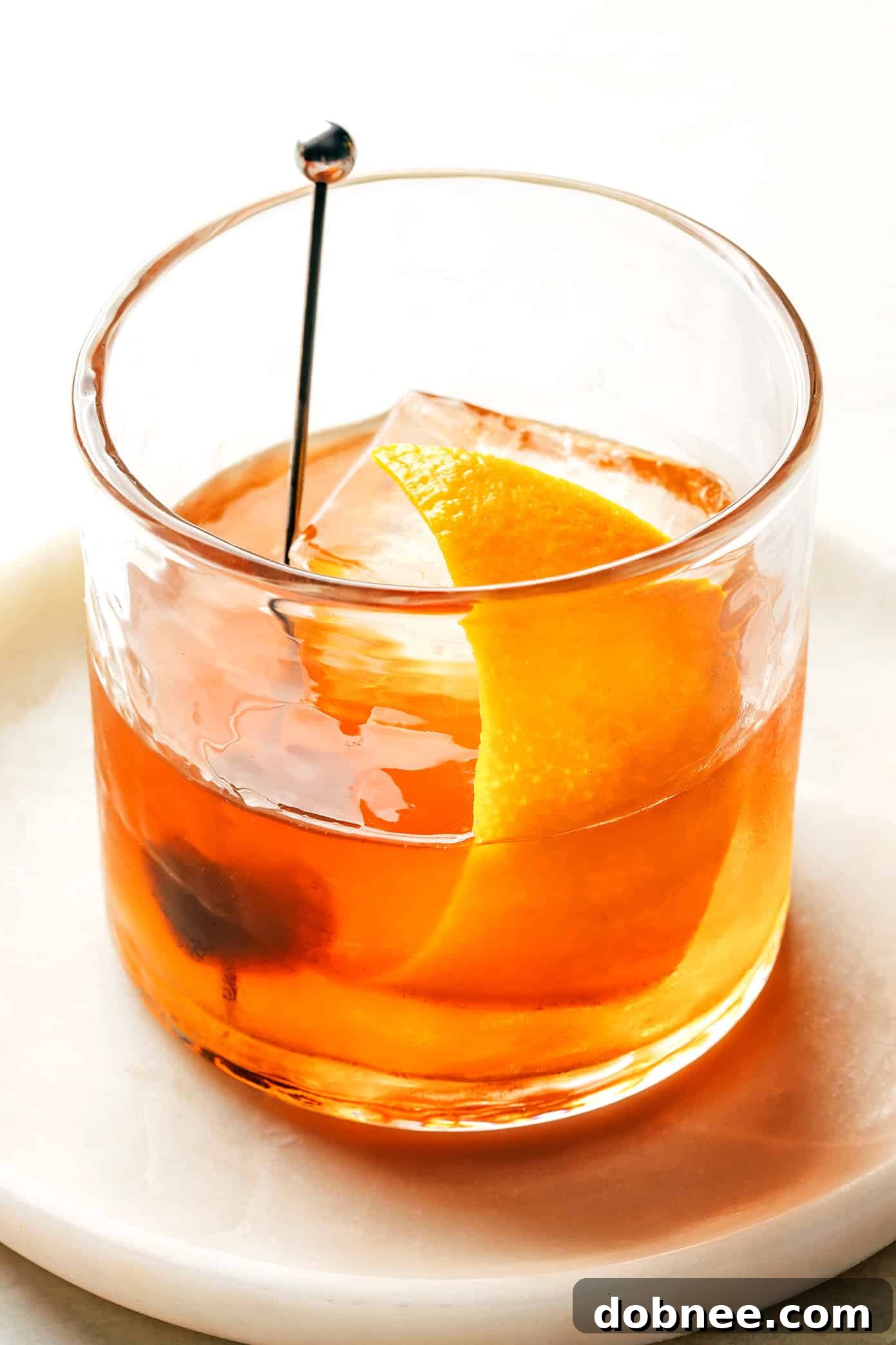 A vibrant Old Fashioned cocktail showcasing its rich amber color, presented in a lowball glass with an orange garnish and a large ice cube, against a warm, inviting background.