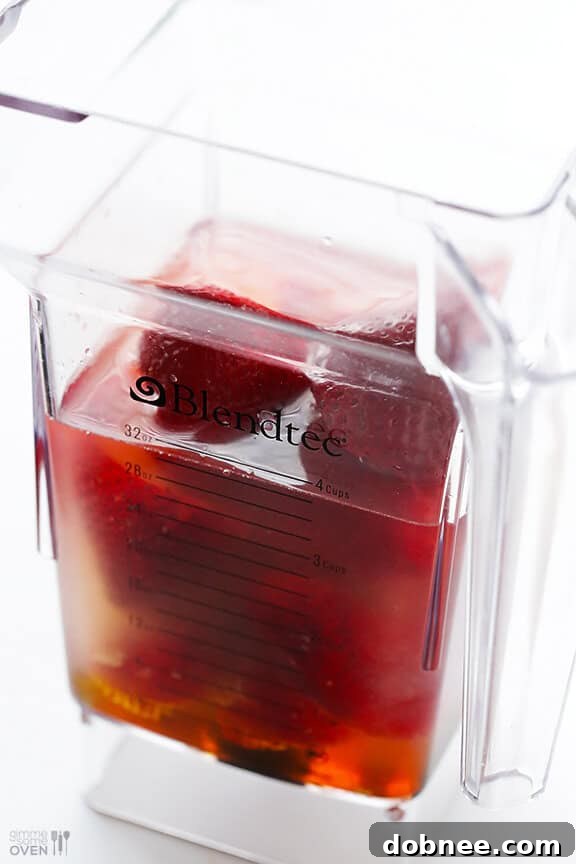 All 5 ingredients for a fresh strawberry margarita laid out: strawberries, tequila, lime juice, honey, and orange liqueur.