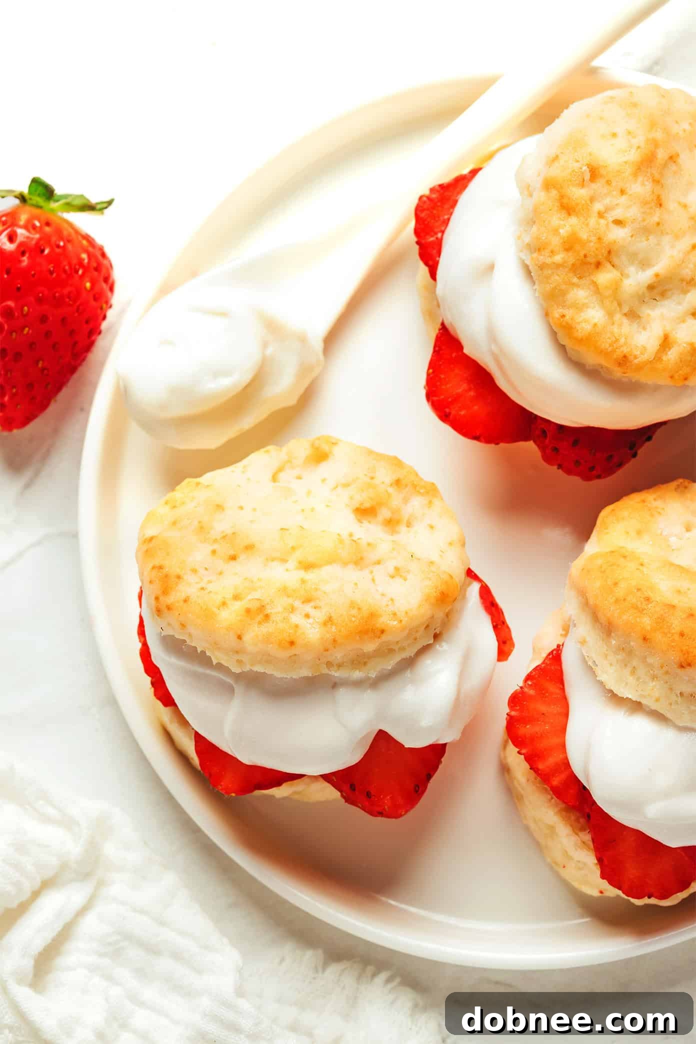 Freshly baked vegan strawberry shortcake topped with bright red strawberries and fluffy coconut whipped cream, glistening under natural light.
