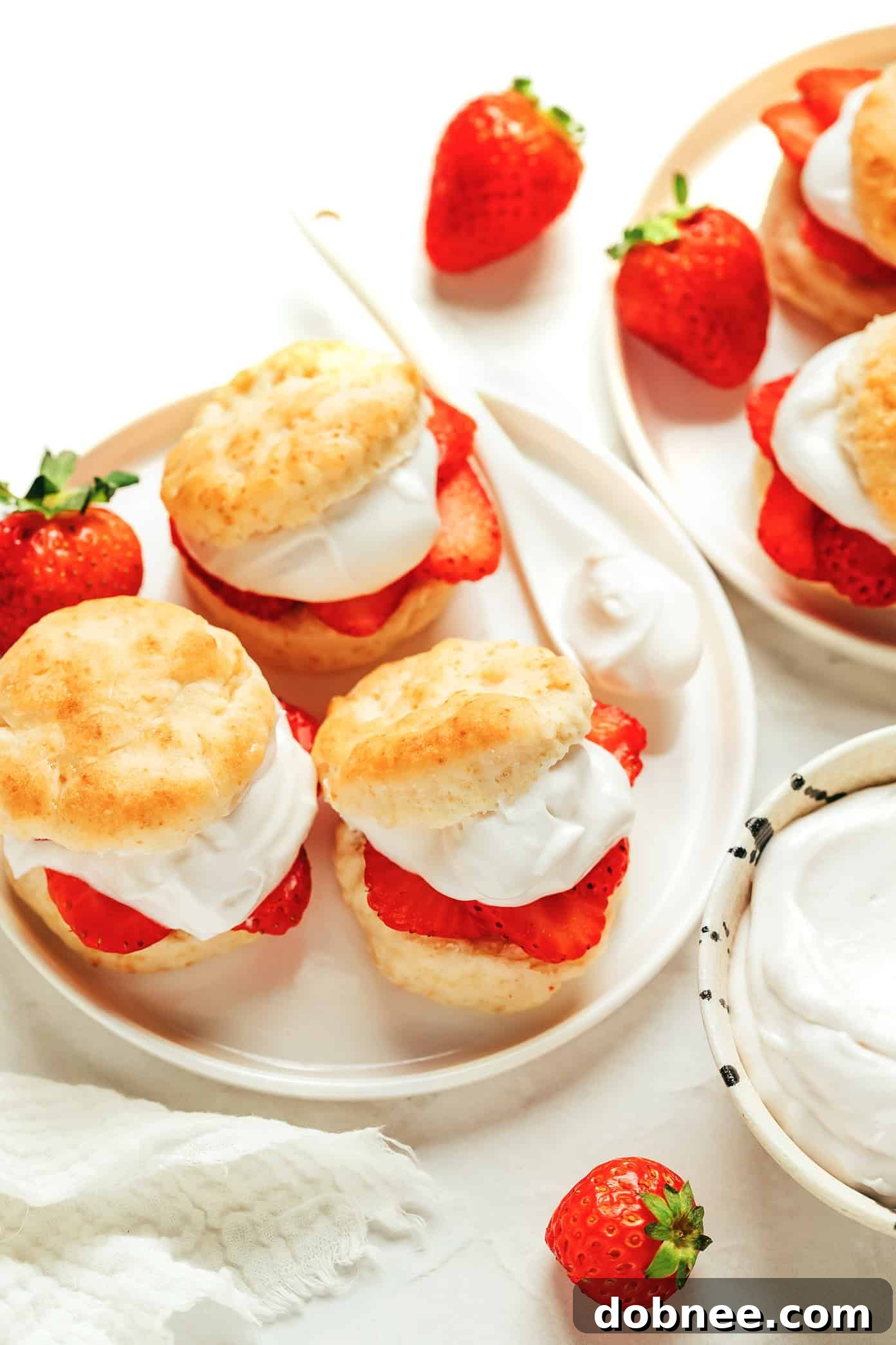 A single serving of vegan strawberry shortcake, beautifully layered with biscuit, strawberries, and coconut whipped cream, on a rustic surface.