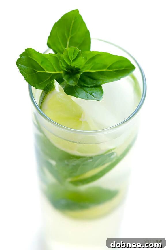 Pouring ginger beer into a glass with muddled mint, lime, and rum to create a Ginger Beer Mojito.