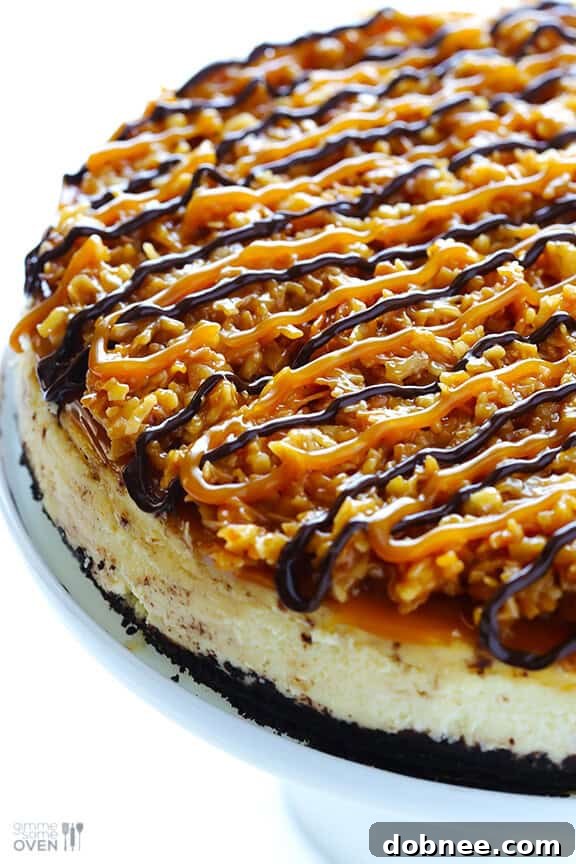 A beautifully sliced Samoa Cheesecake, showcasing layers of Oreo crust, creamy filling, toasted coconut caramel, and chocolate drizzle.