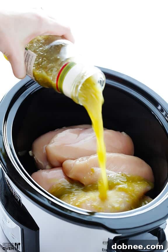 Salsa verde being poured over chicken in a slow cooker
