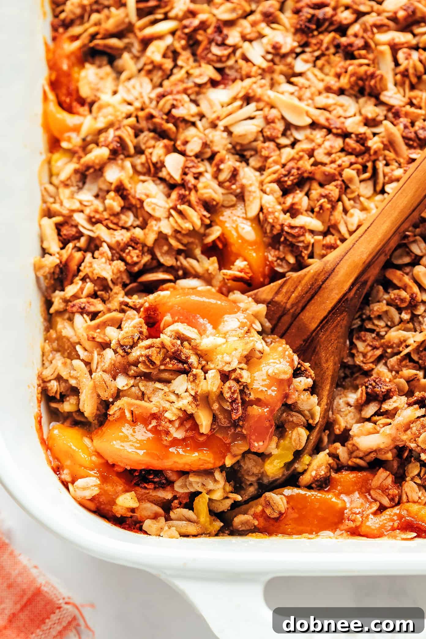 Close-up of a serving of Ginger Peach Crisp with a spoon, showing the gooey fruit filling and crispy topping.