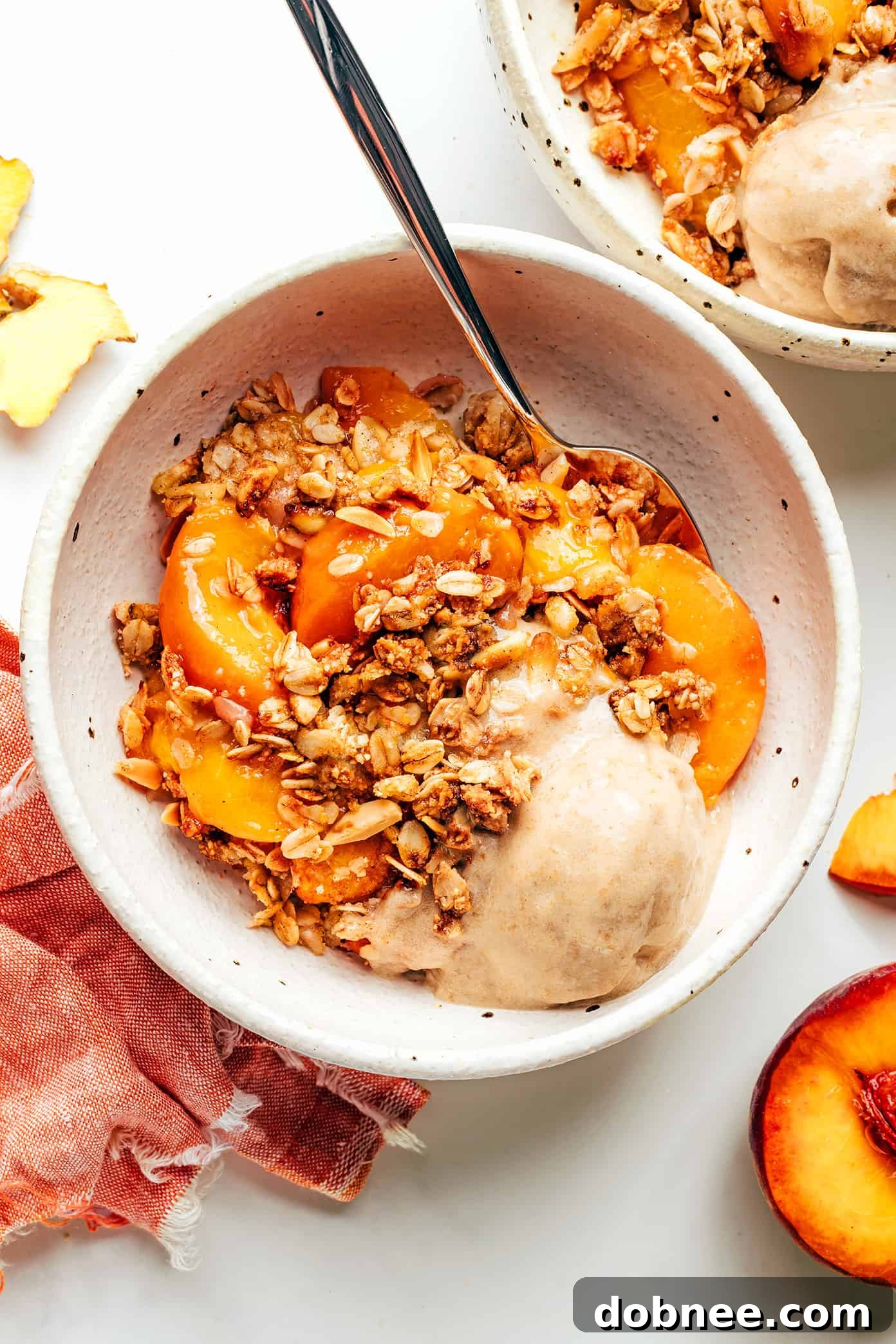 A serving of Ginger Peach Crisp topped with melting vanilla ice cream, ready to be enjoyed.