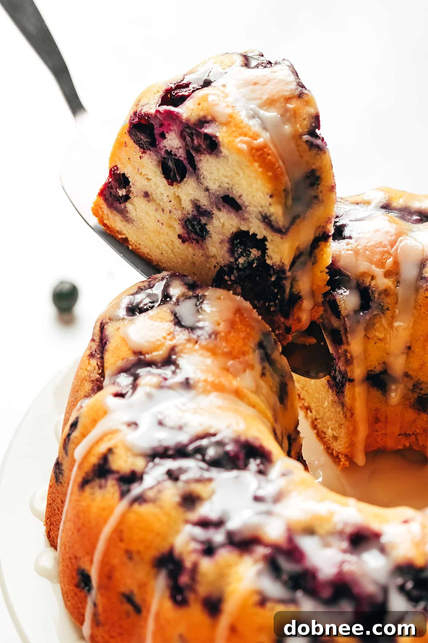 A beautifully baked blueberry bundt cake, golden brown with a light dusting of powdered sugar and fresh blueberries, ready to be sliced.