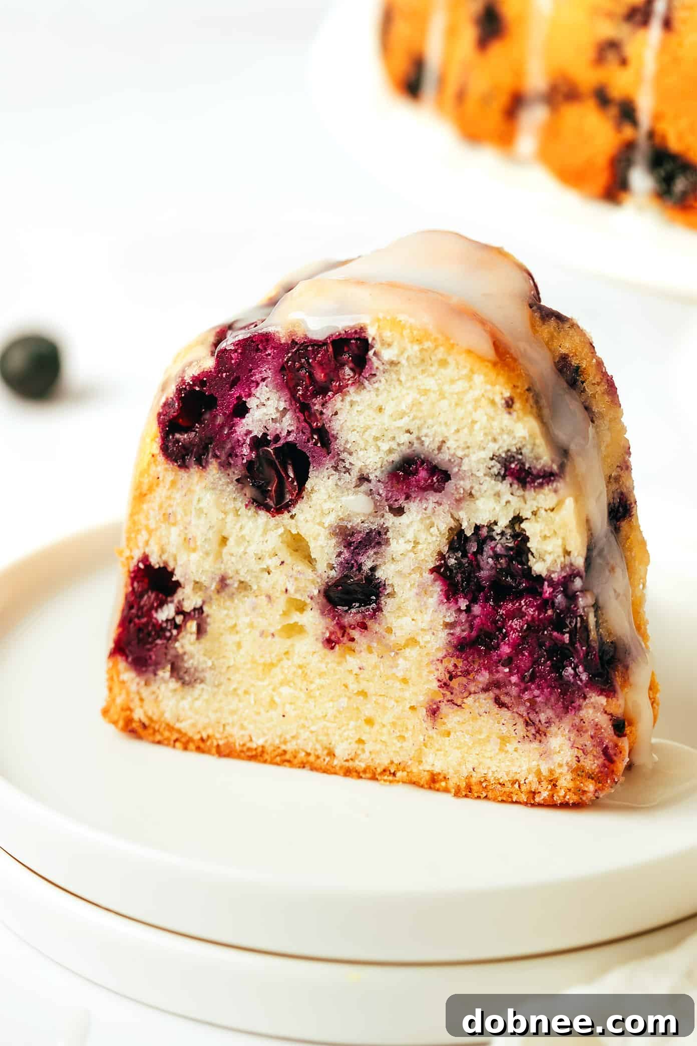 A beautifully composed shot of the blueberry bundt cake, sliced and served on a plate, adorned with extra fresh blueberries and a light drizzle of glaze.