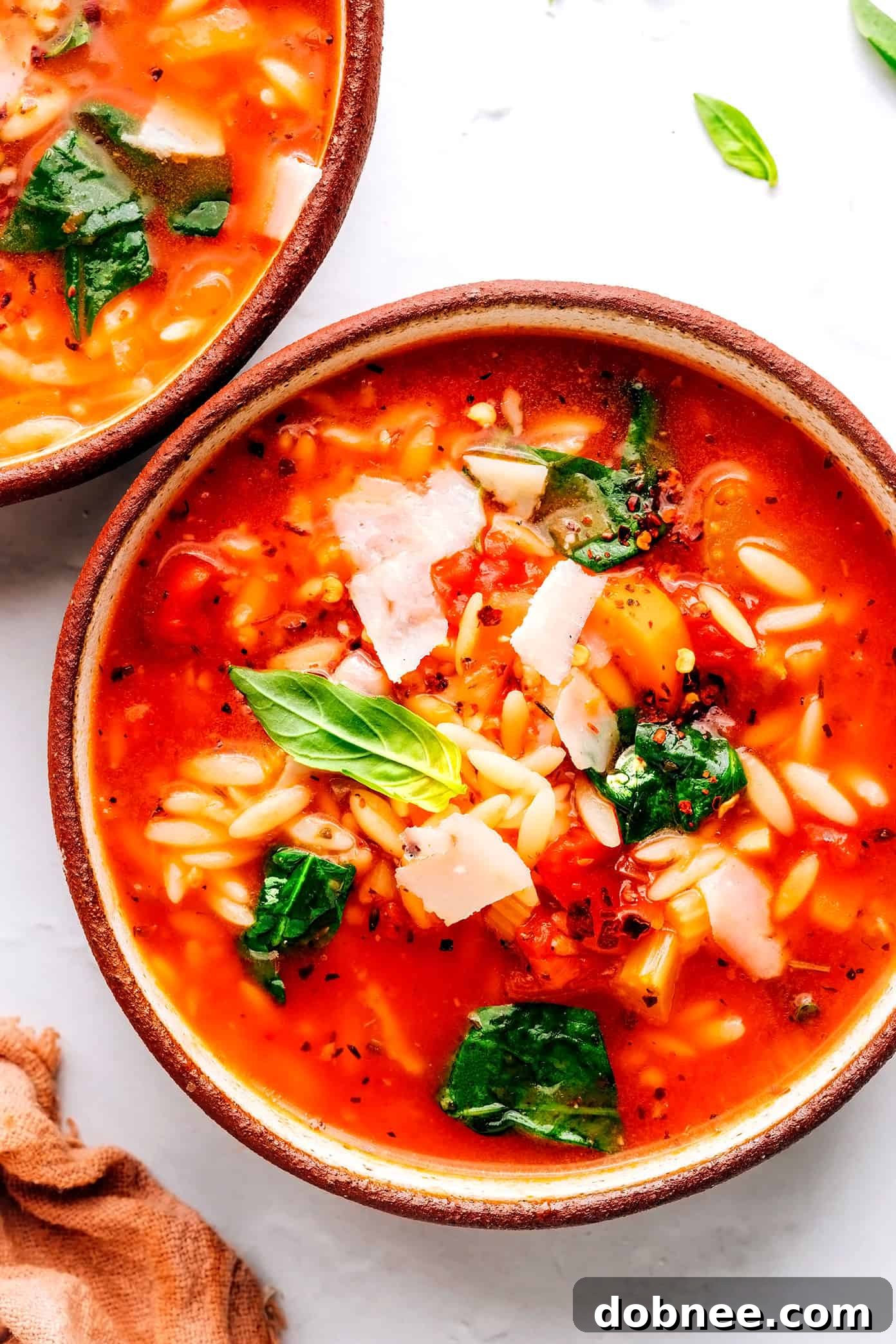 A steaming bowl of Italian Orzo Spinach Soup with fresh basil and Parmesan
