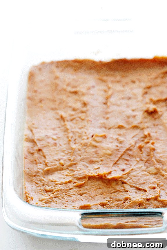 Overhead shot of a partially prepared 7 Layer Dip, showing the distinct layers of beans, guacamole, and sour cream.