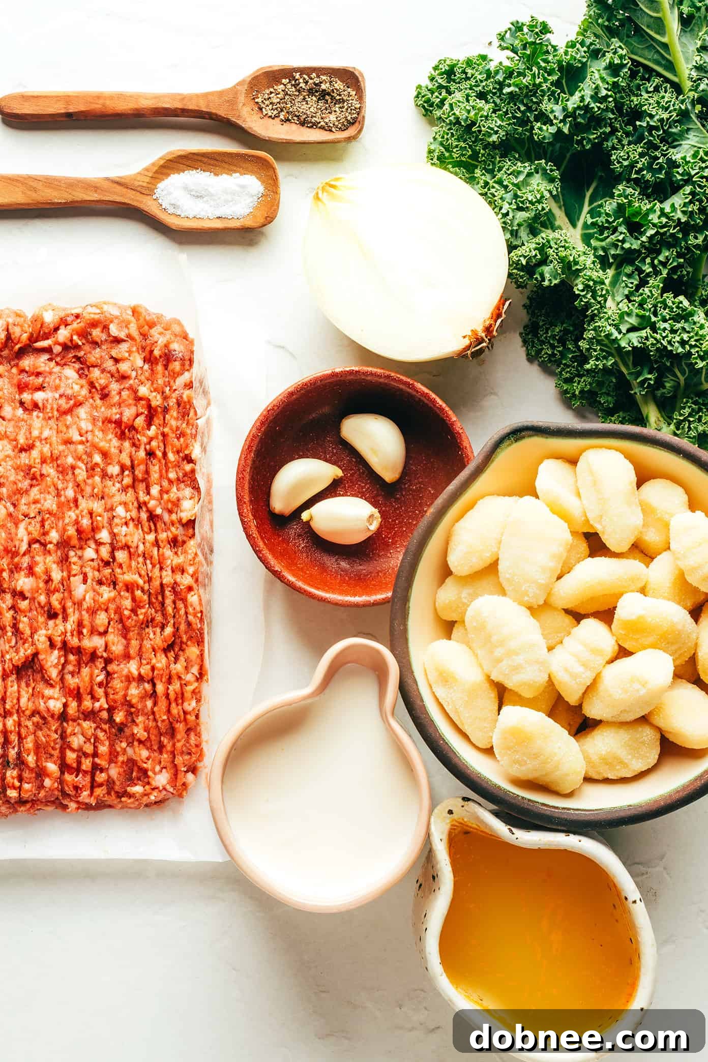 Arrangement of fresh Zuppa Toscana ingredients: Italian sausage, kale, gnocchi, onion, garlic, chicken stock, and heavy cream.