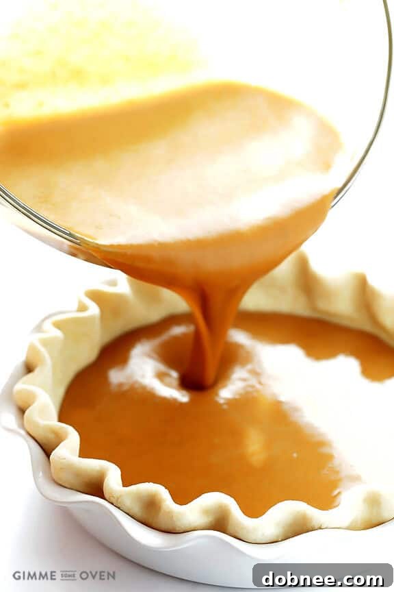 Pouring the smooth bourbon pumpkin pie filling into an unbaked pie crust, a crucial step for a perfect texture.