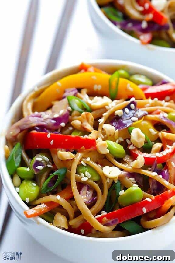A vibrant bowl of rainbow peanut noodles, showcasing an array of colorful vegetables and a rich peanut sauce.