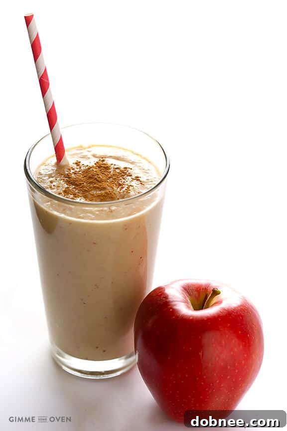 A tall glass of creamy Apple Pie Protein Smoothie, garnished with a sprinkle of cinnamon and a slice of fresh apple, set against a warm, inviting background. It looks incredibly appetizing and healthy.