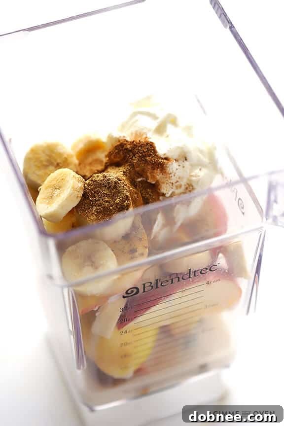 Overhead view of the ingredients for the Apple Pie Protein Smoothie laid out on a clean surface, including fresh apples, a peeled frozen banana, a container of Greek yogurt, and cinnamon sticks.