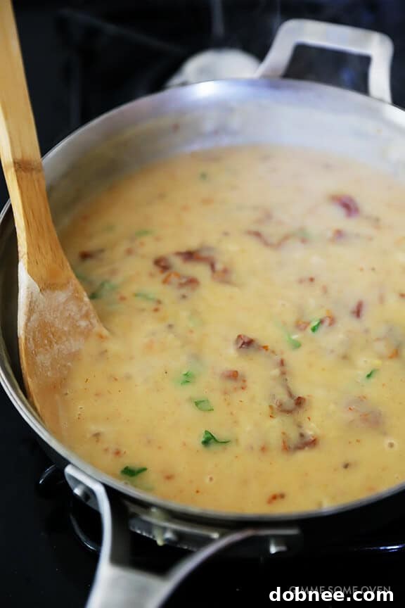 Sun-dried tomatoes and fresh basil being stirred into the creamy sauce