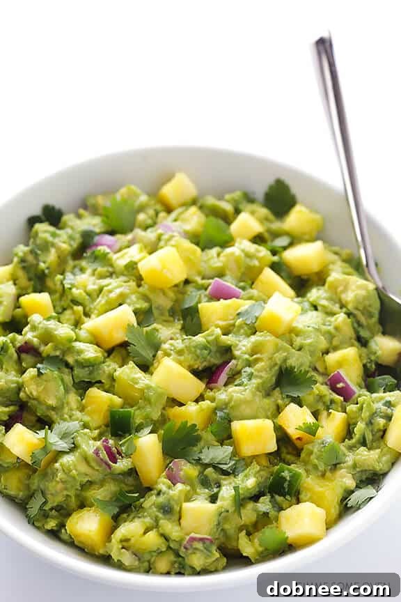 A large serving bowl filled with creamy pineapple guacamole, garnished with fresh pineapple chunks and cilantro leaves, ready to be enjoyed.