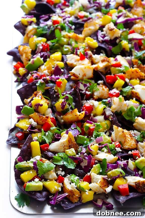 Kaleidoscope Fish Taco Nachos 3 Close-up of vibrant Rainbow Fish Taco Nachos on a serving plate, showcasing colorful mango slaw, seasoned fish, and melted cheese.