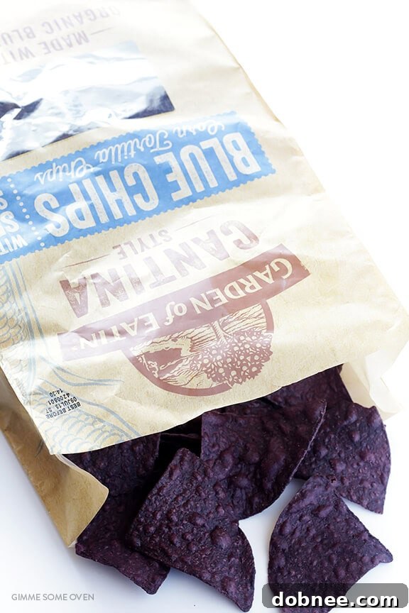 Kaleidoscope Fish Taco Nachos 4 Preparing Rainbow Fish Taco Nachos: Blue corn tortilla chips piled on a baking sheet with shredded Monterrey Jack cheese, ready for broiling.